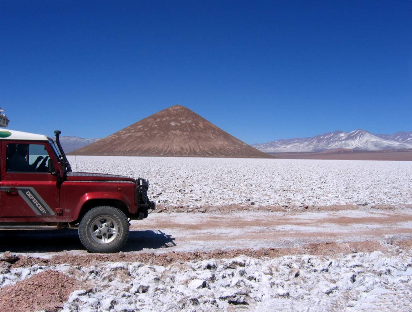 Land Rover Defender am Rand einer Salzfläche in Argentinien vor einem kegelförmigen Berg