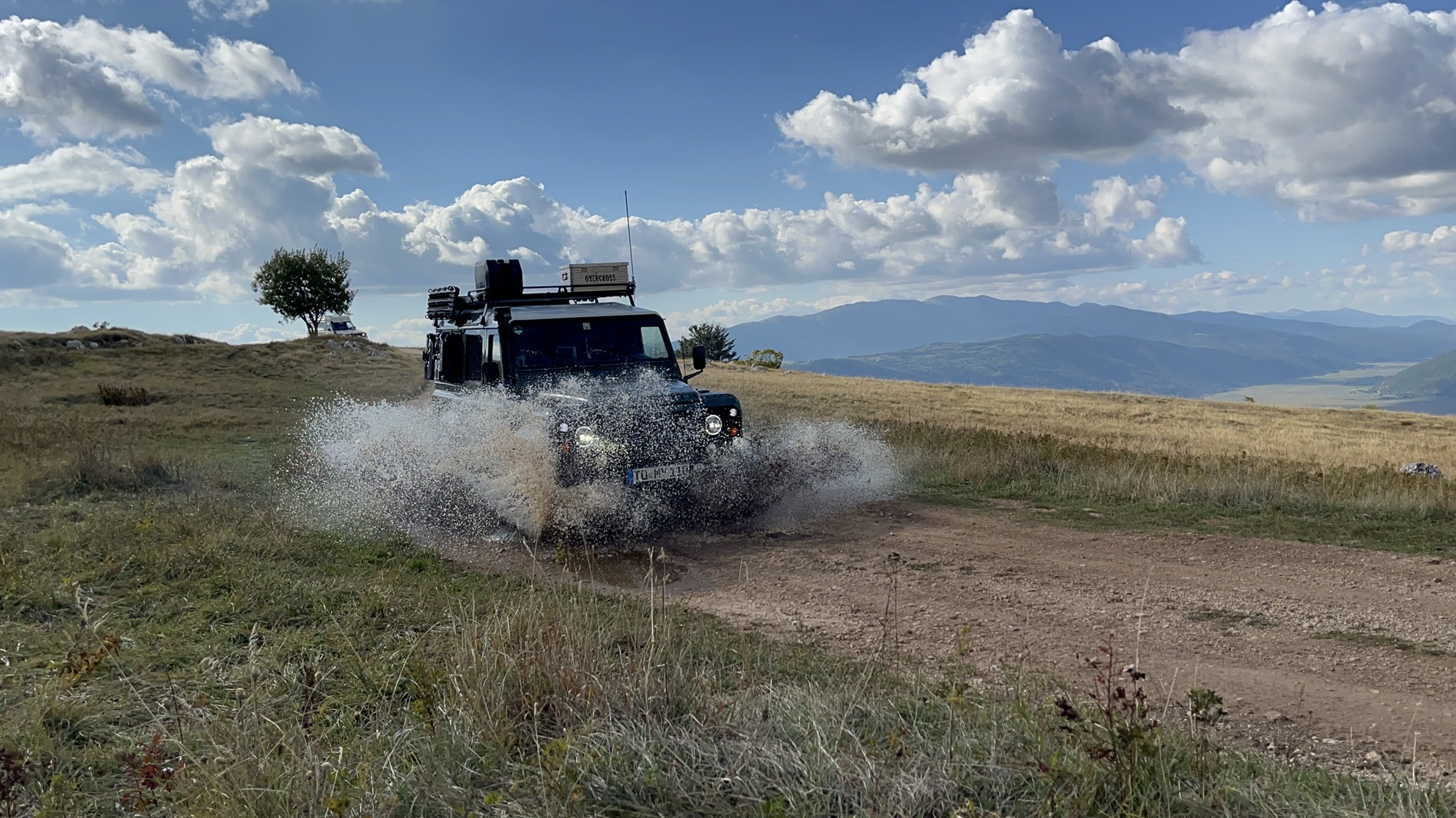 Land Rover Defender mit Dachträger durchfährt eine Pfütze auf einem Bergweg in Bosnien