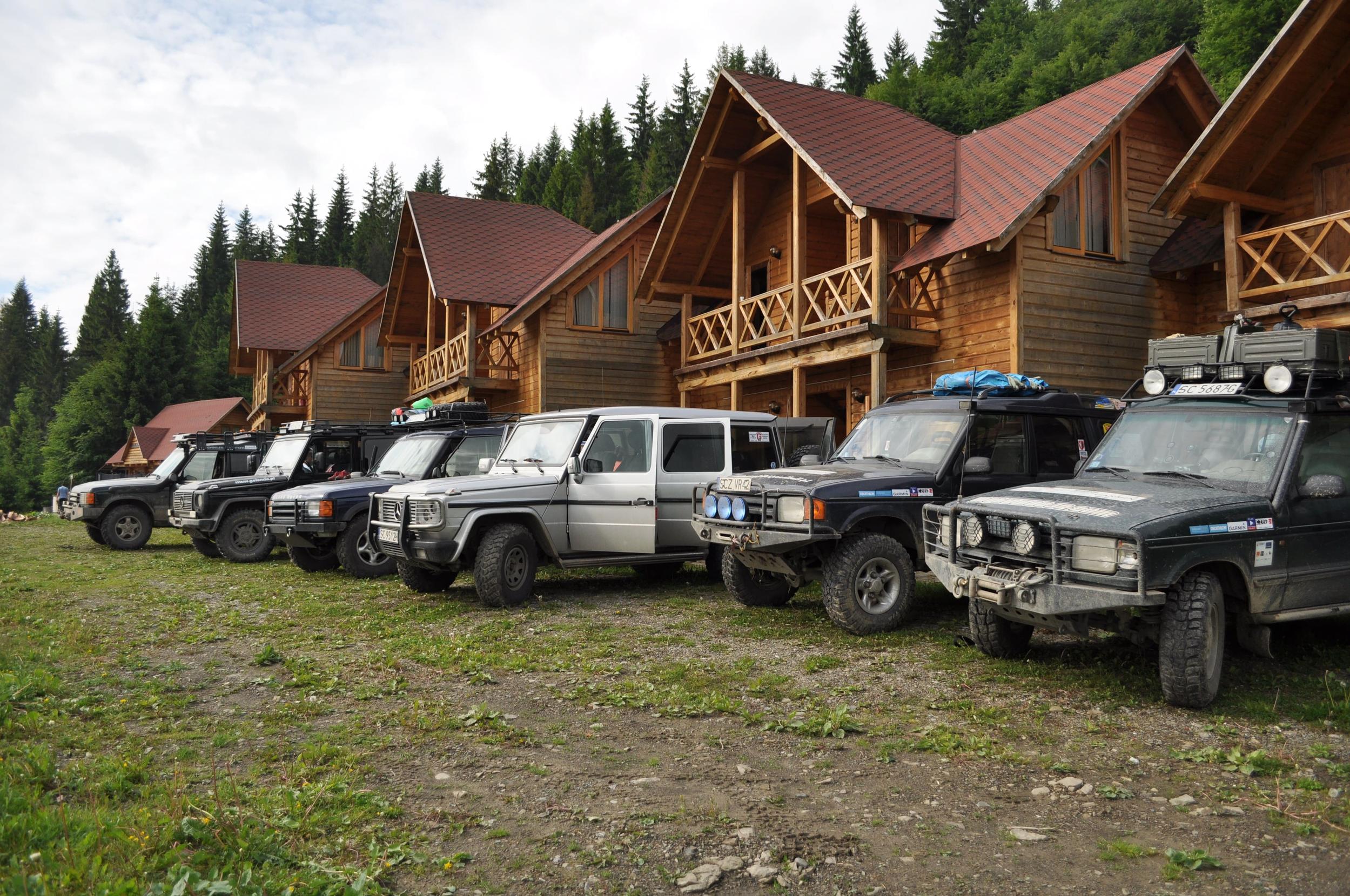 4x4-Fahrzeuge vor rustikalen Holzhütten in den ukrainischen Karpaten.