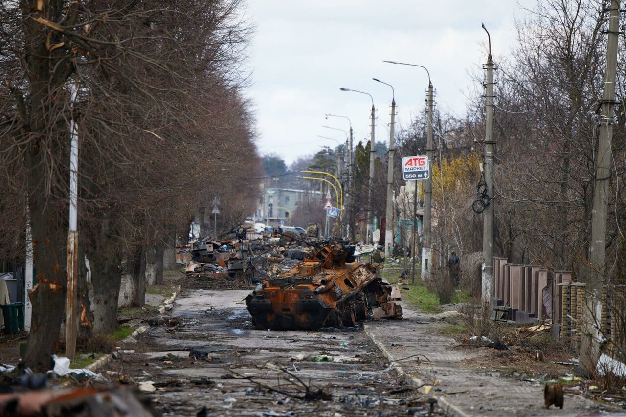 Das Wrack eines ausgebrannten Panzerfahrzeugs mitten auf einer Straße gesäumt von kahlen Bäumen