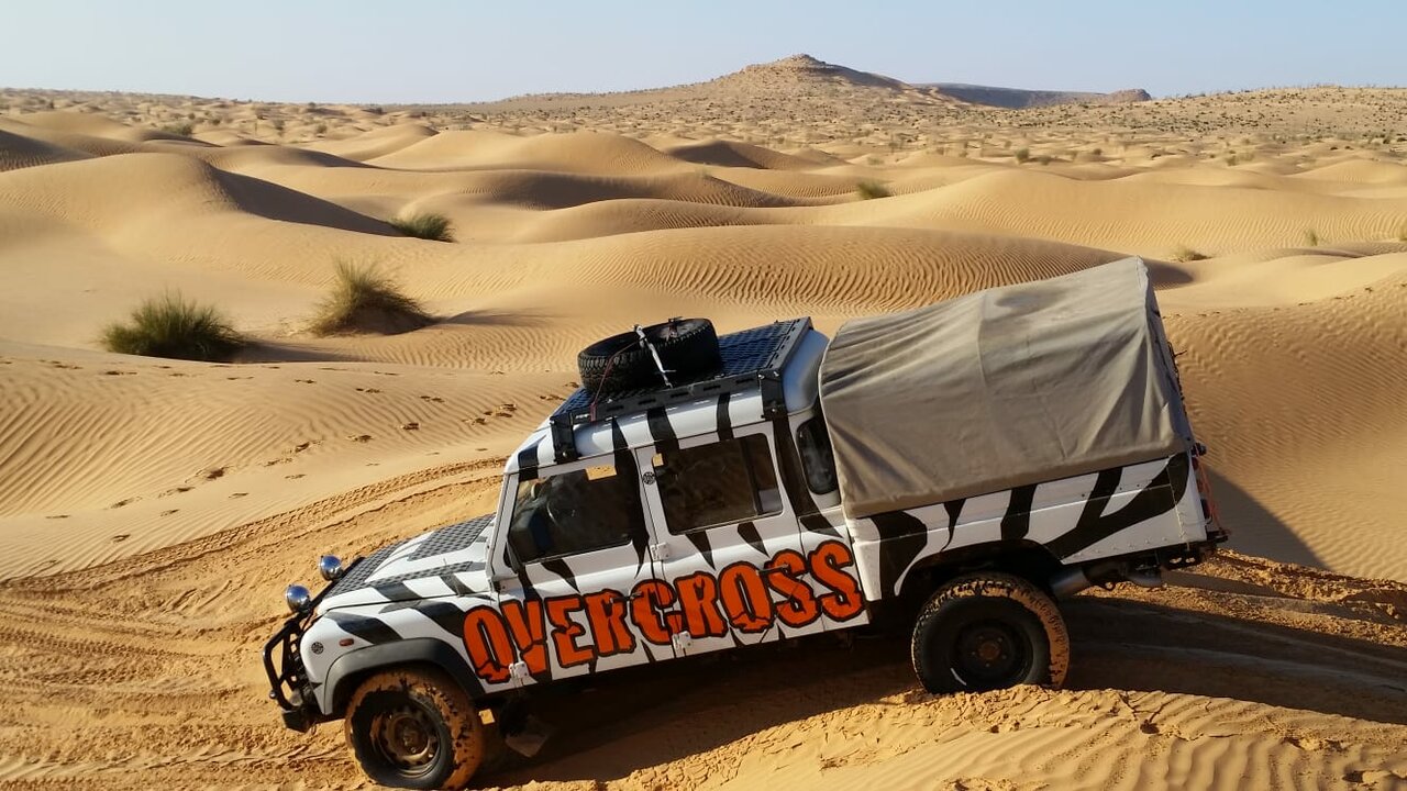 Ein 4x4 mit Overcross-Logo und Zebrastreifen-Lackierung steht auf einer Wüstendüne