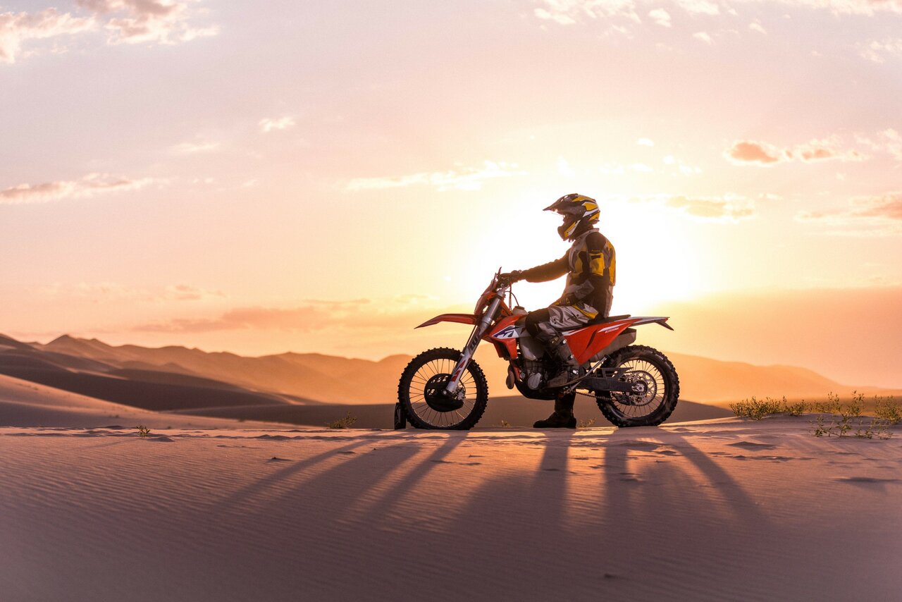 Ein Fahrer auf einem Enduro-Motorrad zeichnet sich auf einer Sanddüne gegen die untergehende Sonne ab