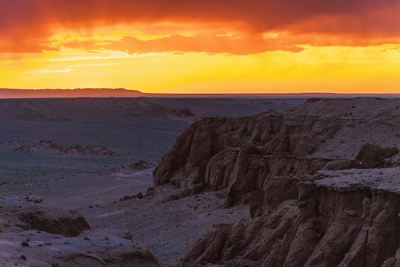 Ein dramatischer oranger Sonnenuntergang über erodierten Wüstenklippen und Schluchten in der Gobi