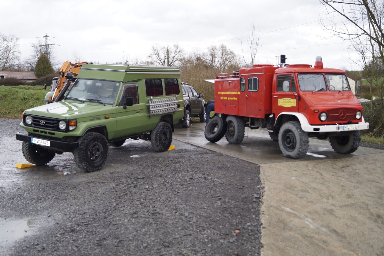 A green off road 4x4 parked beside a red Mercedes Unimog service truck marked Markom