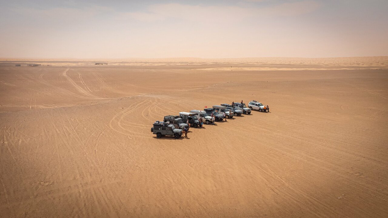 Aerial view of a line of 4x4 vehicles parked diagonally across a vast desert plain