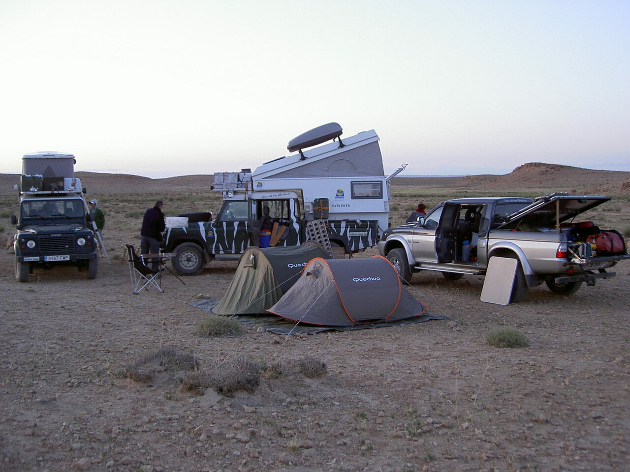 Land Rover Defender und ein Wohnmobil stehen bei Sonnenuntergang neben zwei Zelten im Wüstencamp