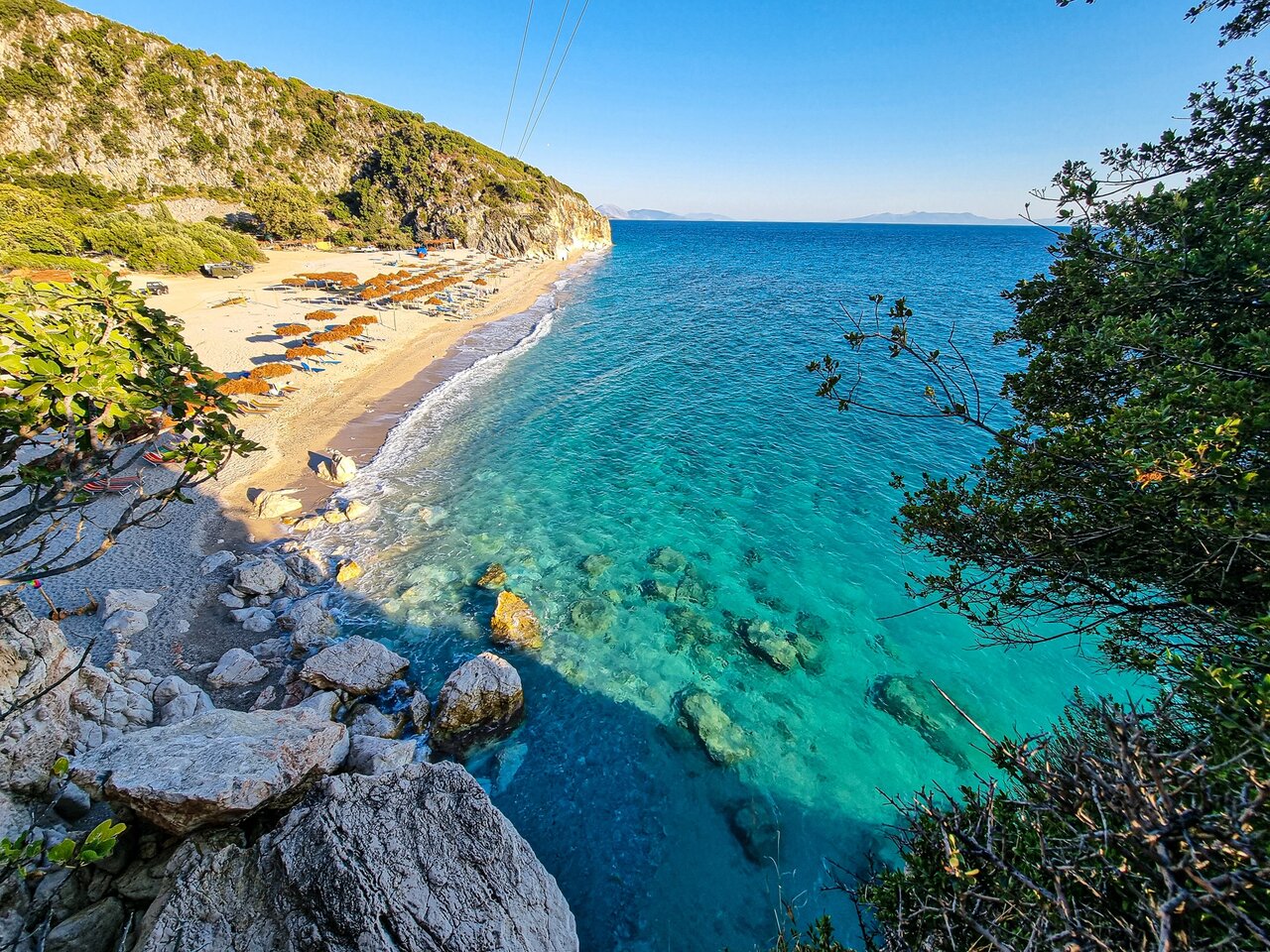Türkisfarbener Strand in einer Bucht mit Klippen und Reihen von Sonnenschirmen