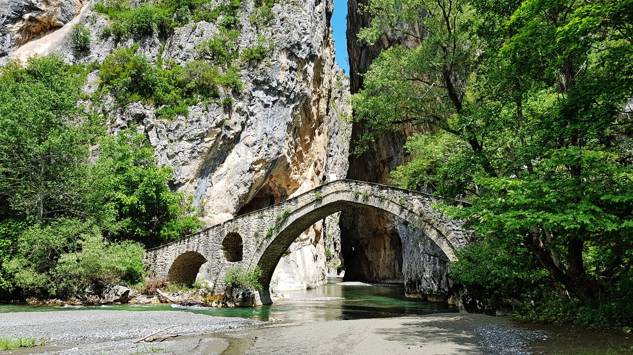Antiga ponte de pedra em arco sobre um rio turquesa num desfiladeiro florestado verde