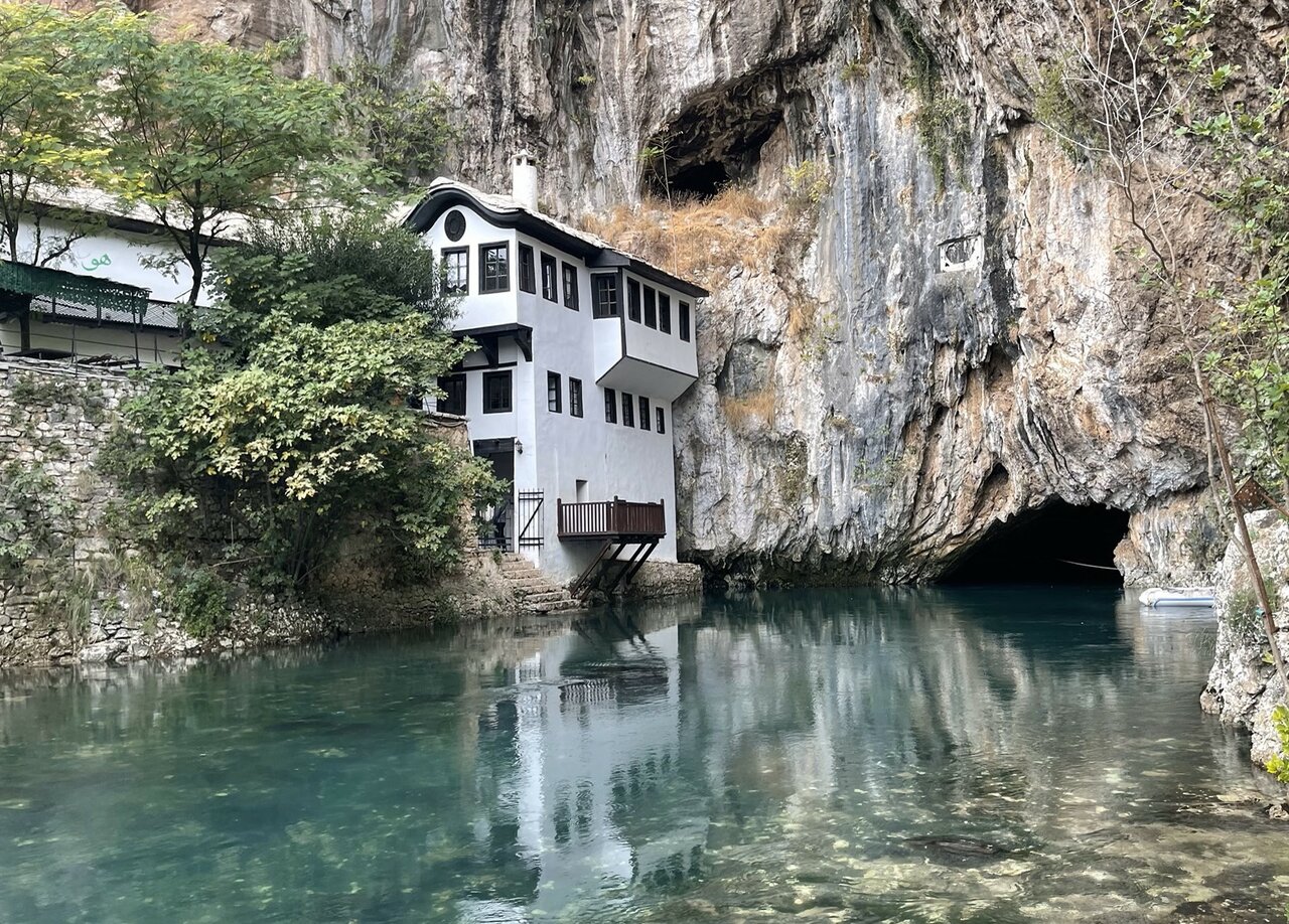 Ein weißes Haus in einen Kalksteinfelsen gebaut, über einer türkisfarbenen Flussquelle
