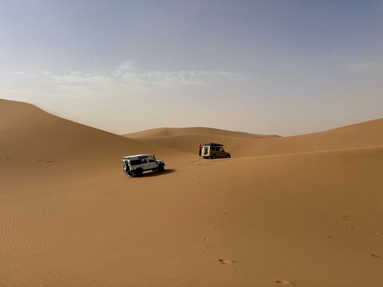 Zwei 4x4 und eine Person stehen zwischen großen Sanddünen