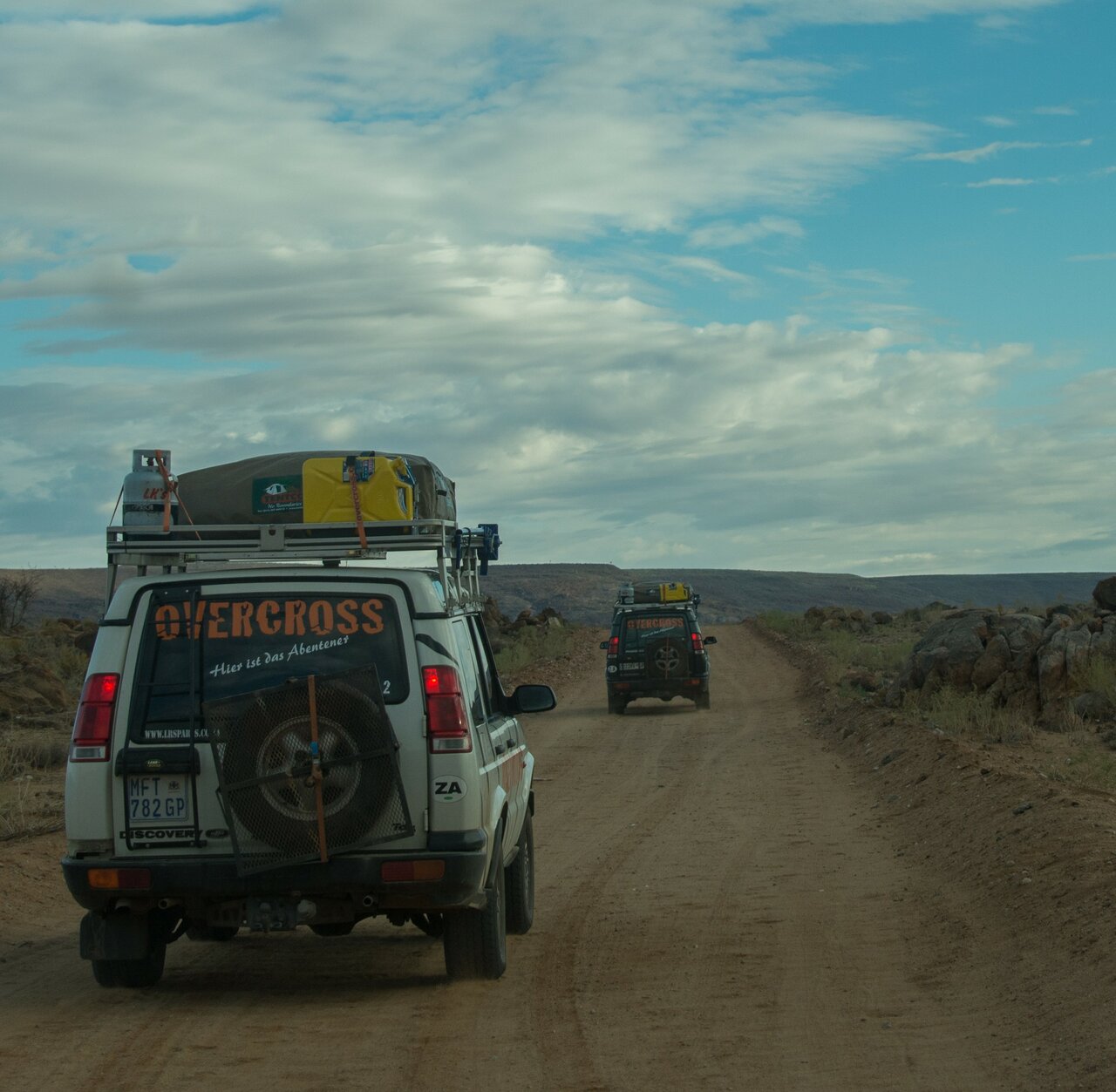 Dois 4x4 da Overcross circulam em comboio por um caminho de terra entre colinas rochosas