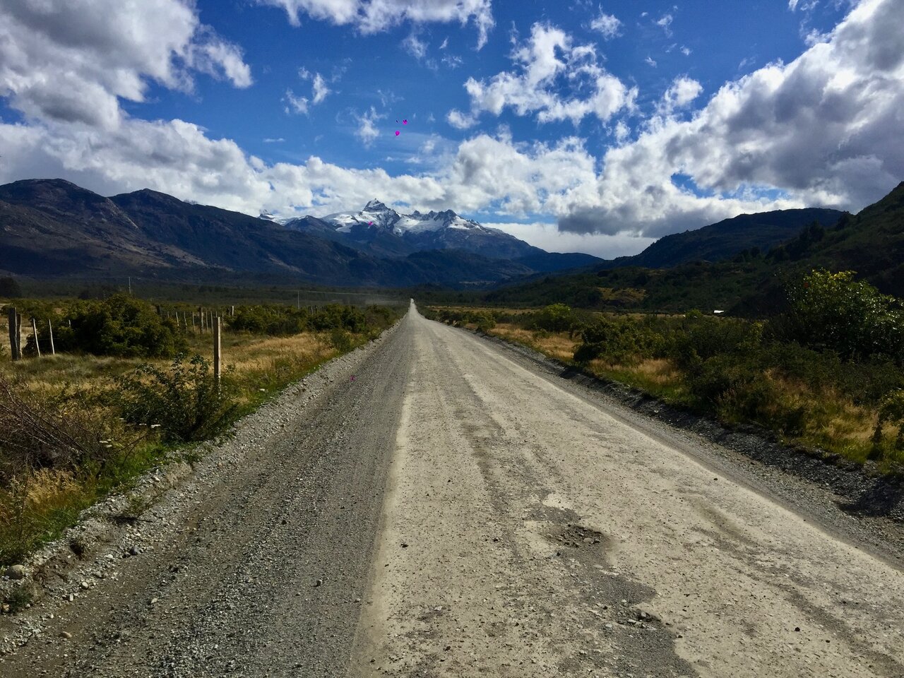 A gravel road leading toward snow-capped mountains in a wide valley