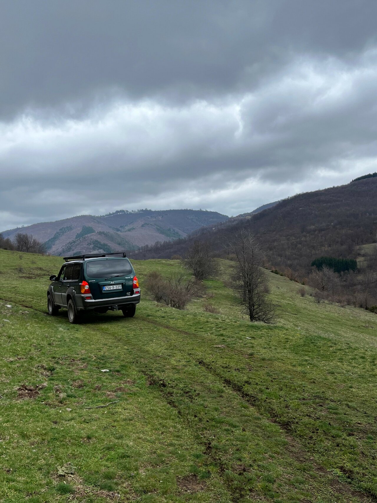 Ein grüner 4x4-SUV steht auf einem grasbewachsenen Hang unter einem stürmischen Himmel