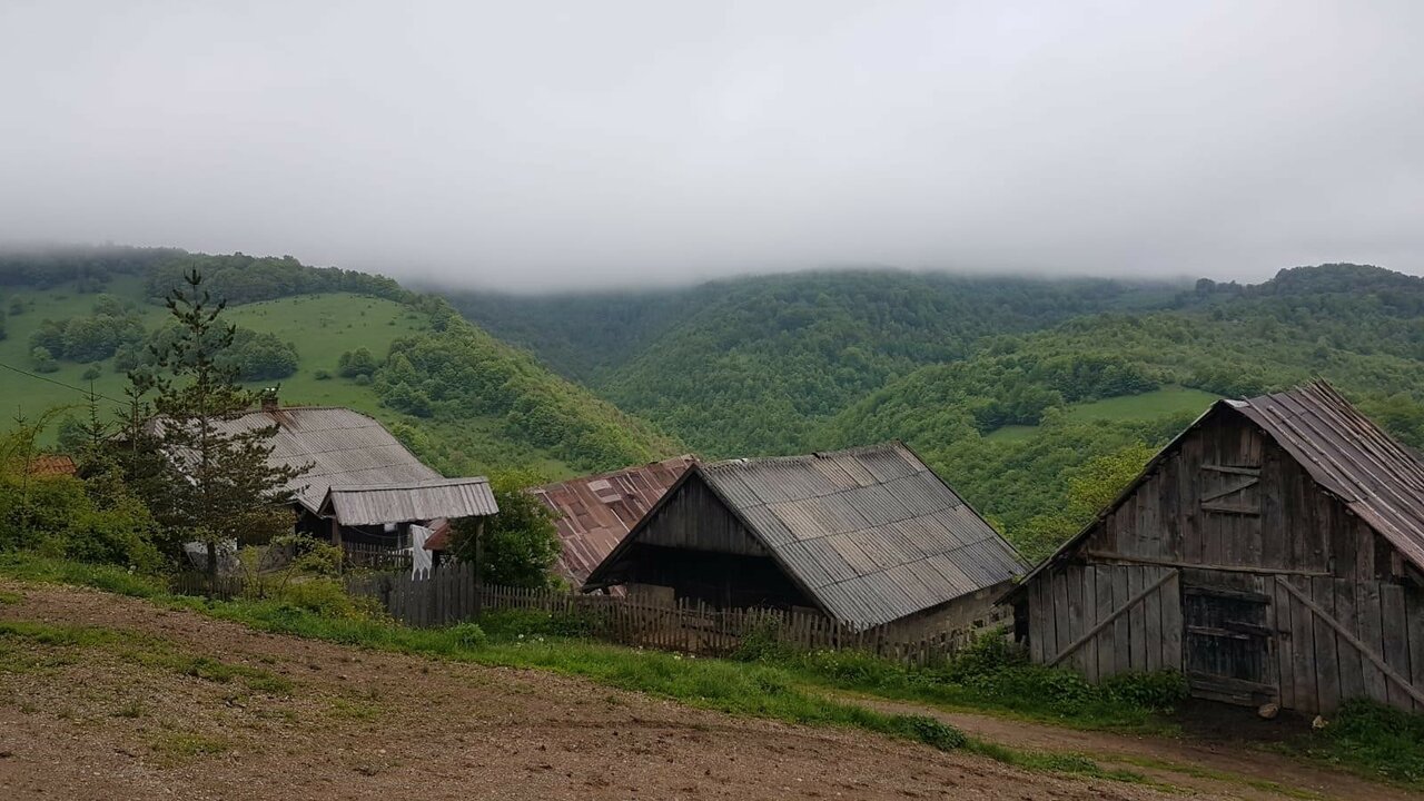 Traditionelle Holzgebäude eines Hofs mit Schindeldächern in einem nebligen grünen Tal