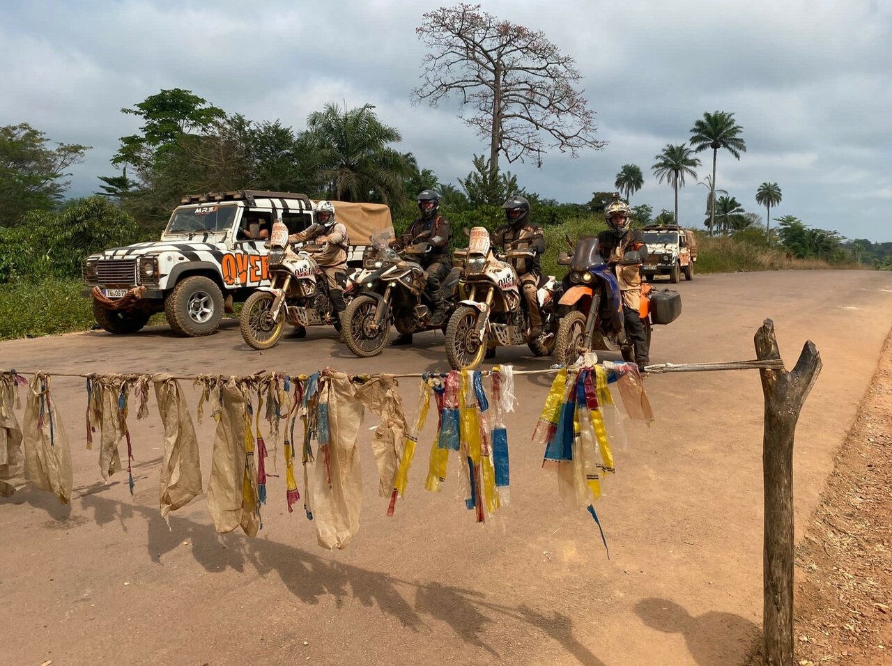 Motos e um caminhão de apoio parados num posto de controle à beira da estrada, com tiras de plástico penduradas