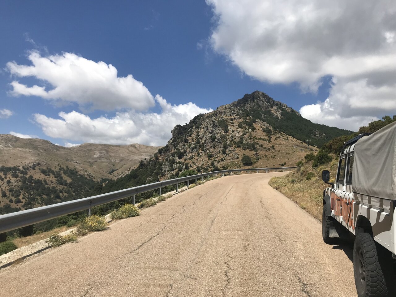 Mountain road with a rocky peak ahead and the rear of an off-road vehicle at the frame edge