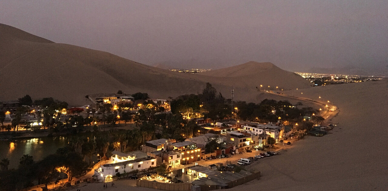 A desert oasis town lit up at night among tall sand dunes