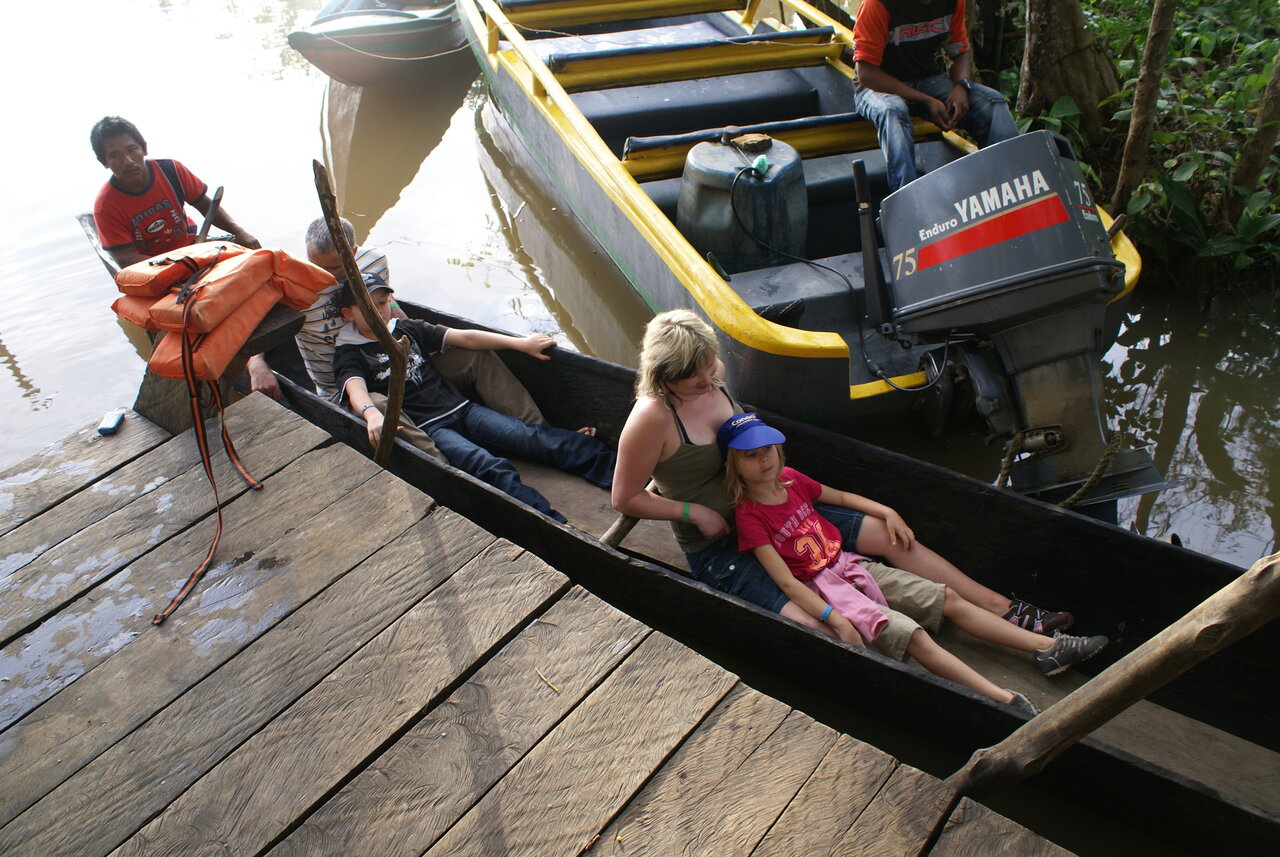 Eine Familie sitzt in einem Holzkanu an einem Steg neben einem Boot mit Yamaha-Außenbordmotor