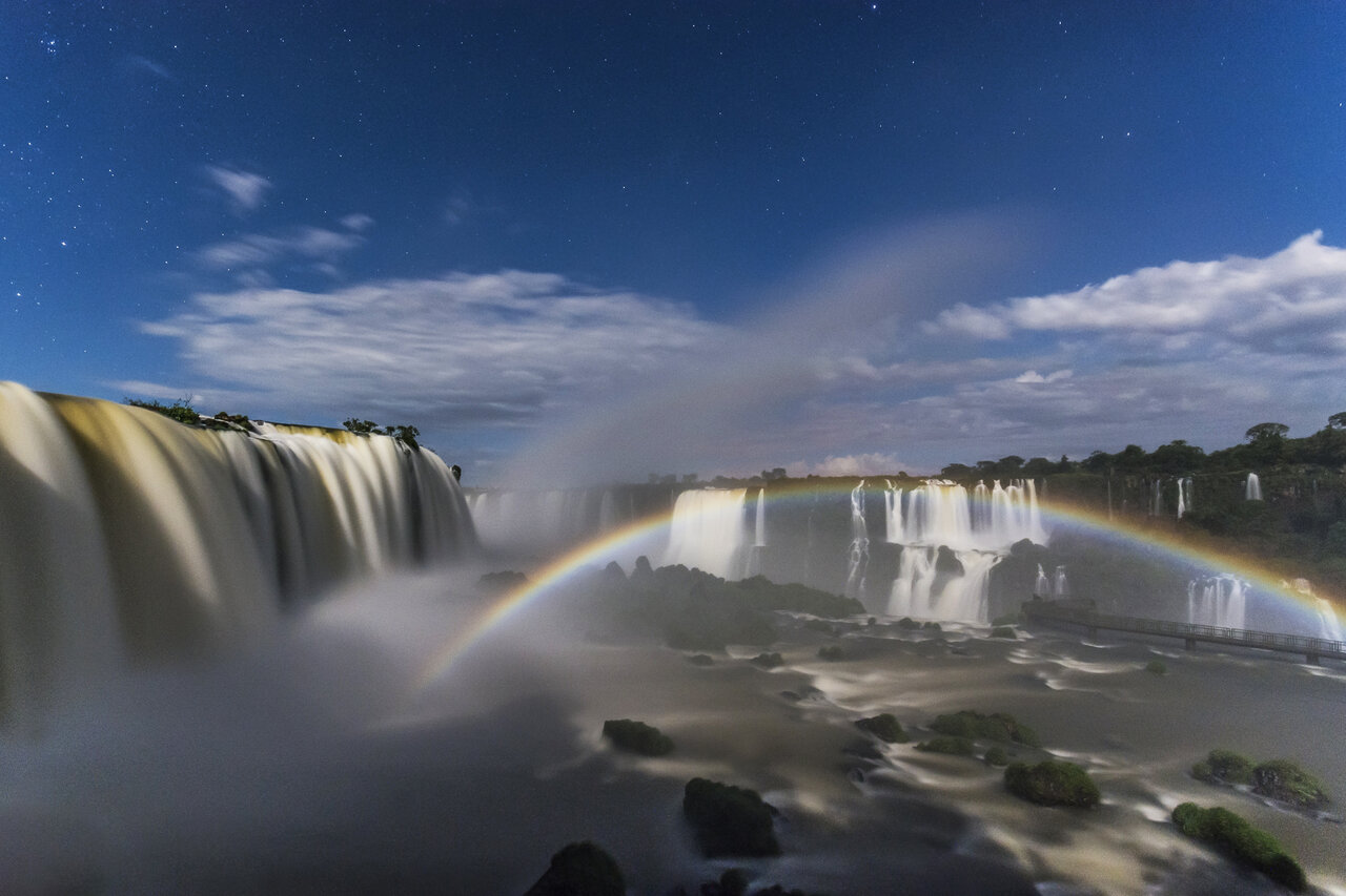 Iguazu-Wasserfälle bei Nacht mit einem vollständigen Regenbogen über den Kaskaden unter einem Sternenhimmel