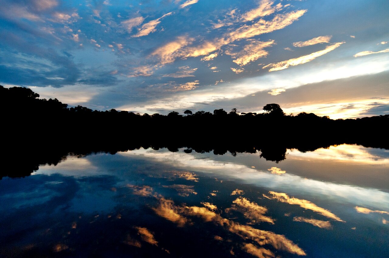 El cielo del atardecer reflejado en un río en calma, con la silueta oscura del bosque en el horizonte