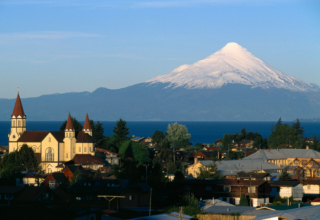 Eine Kirche mit zwei Türmen am See in Puerto Varas, gegenüber ein schneebedeckter Vulkan