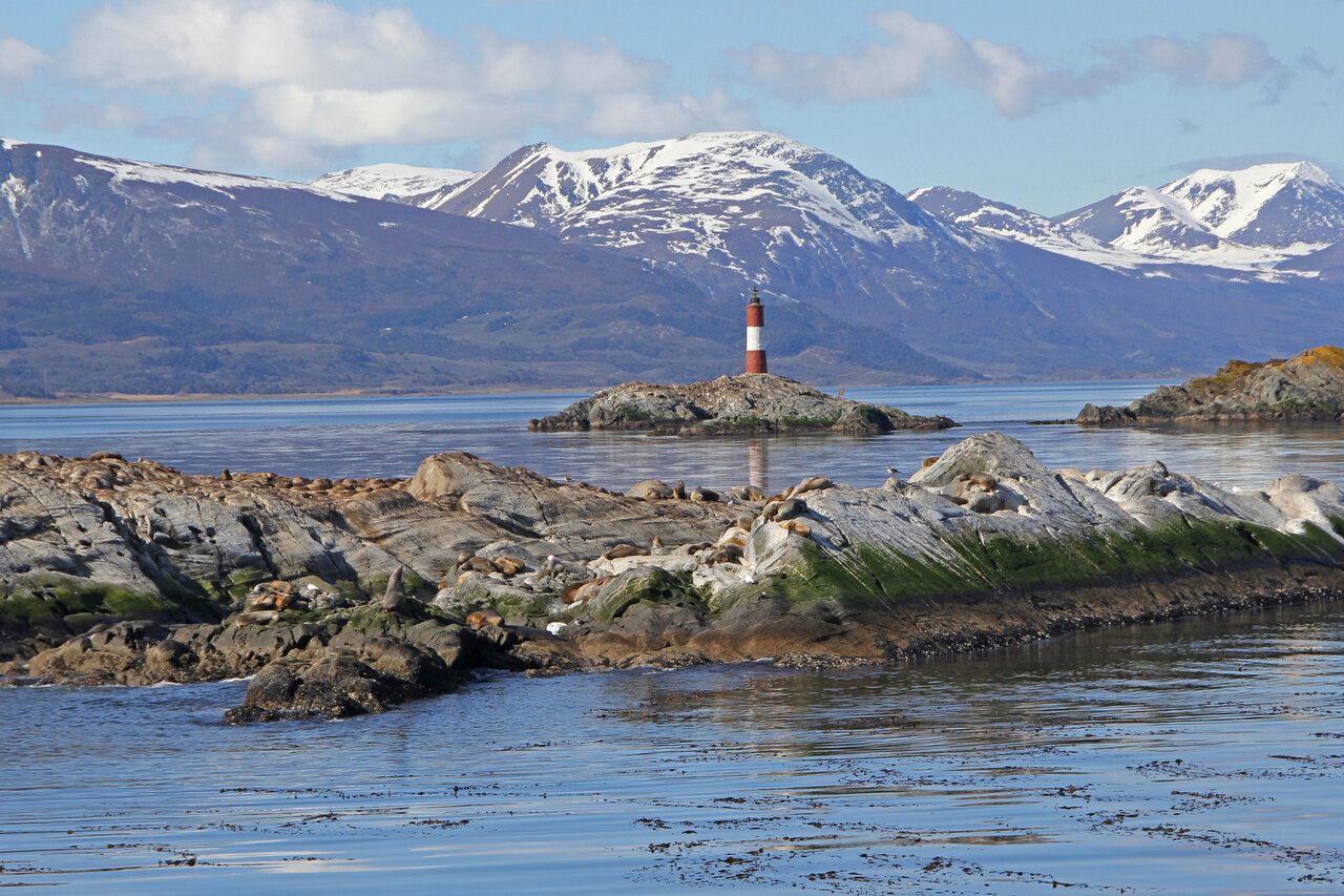 Ein Leuchtturm auf einer kleinen felsigen Insel, dahinter schneebedeckte Berge