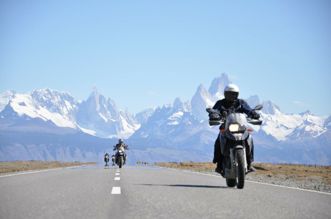 Motorradfahrer fahren eine asphaltierte Straße, dahinter die zerklüfteten Granitspitzen des Fitz Roy Gebirges