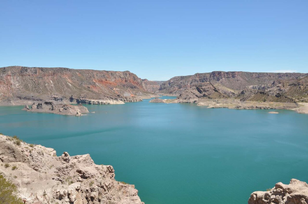Ein türkisfarbenes Reservoir zwischen roten Felswänden einer Schlucht, klarer blauer Himmel darüber