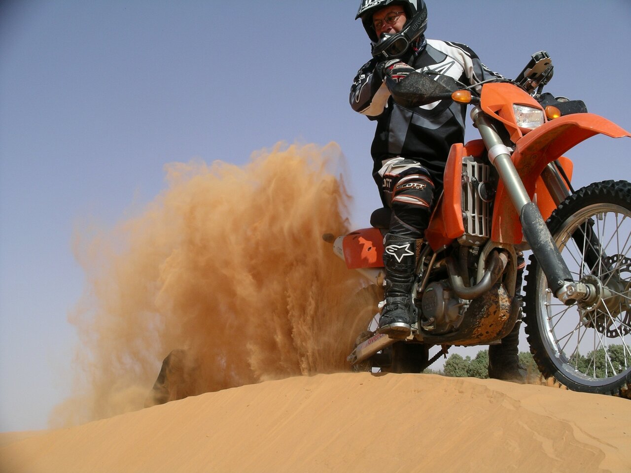 Um piloto numa moto de enduro laranja levanta um jato de areia