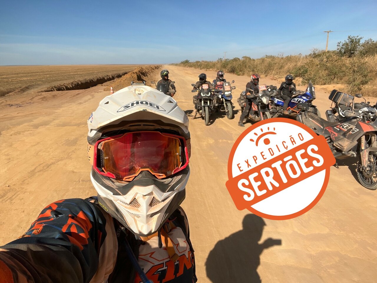 Selfie eines Fahrers mit Motorrädern und Fahrern auf einer Feldstraße, großes Expeditionslogo im Bild