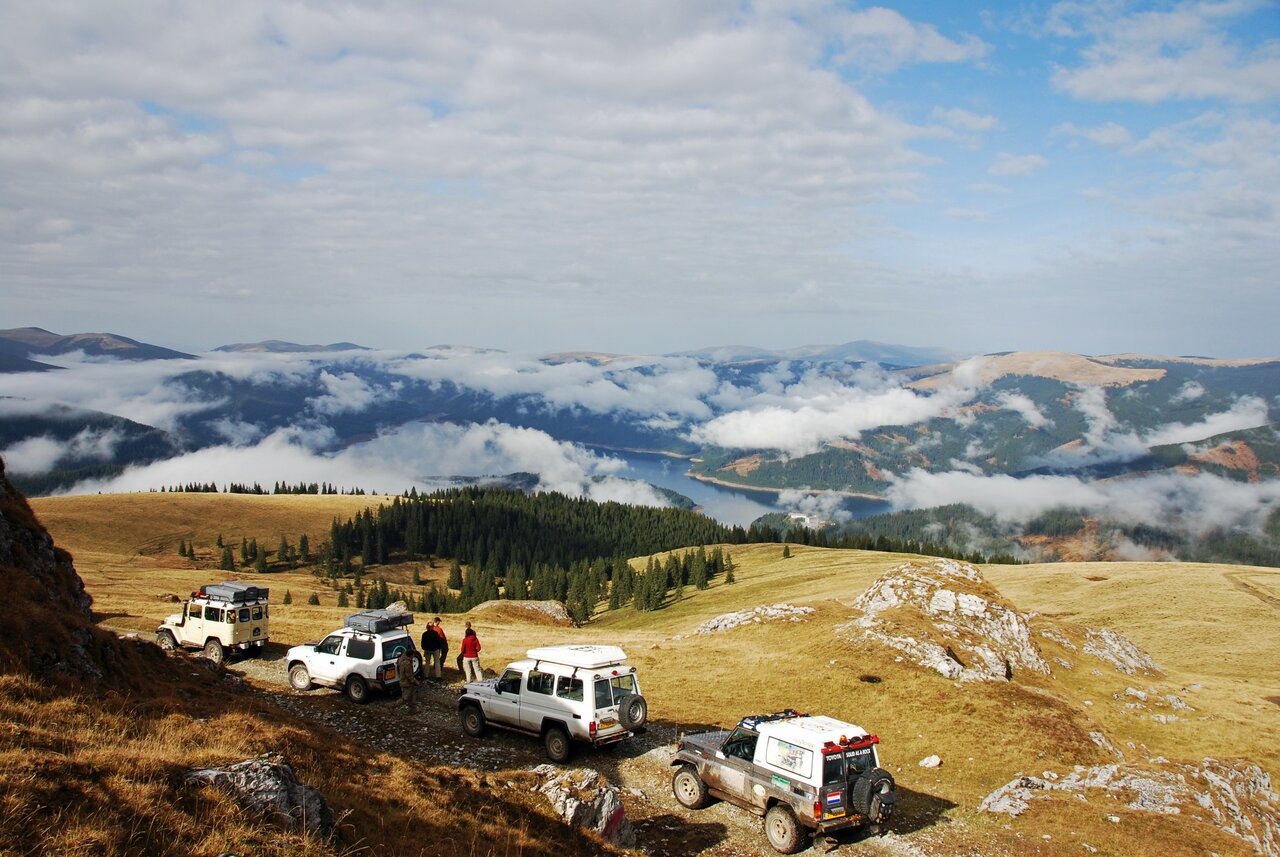 Cuatro vehículos 4x4 blancos aparcados en una cresta cubierta de hierba sobre un lago en un valle con niebla