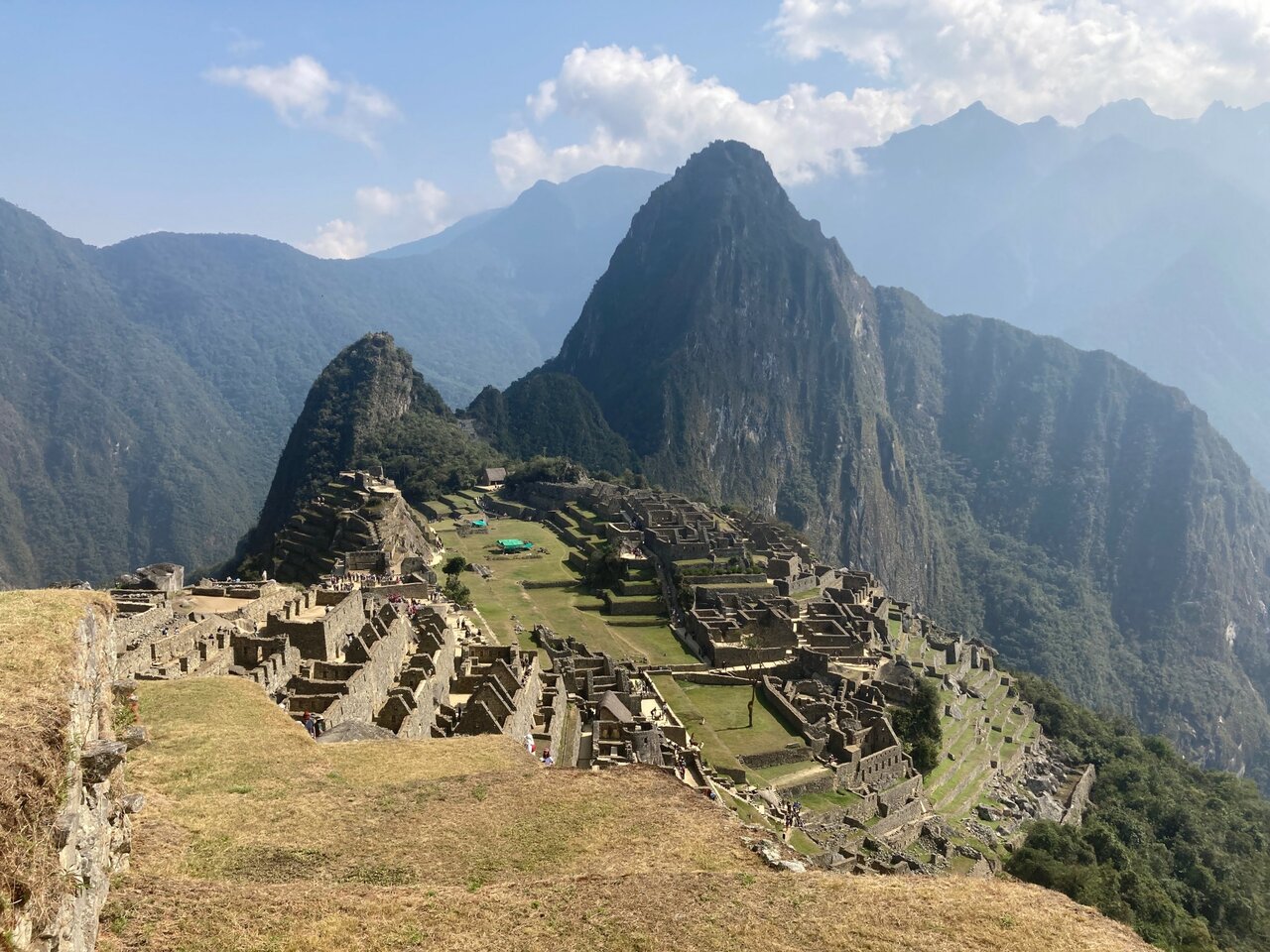 Ruinen von Machu Picchu auf einem Bergrücken, Touristen laufen über die Terrassen, dahinter der Huayna Picchu