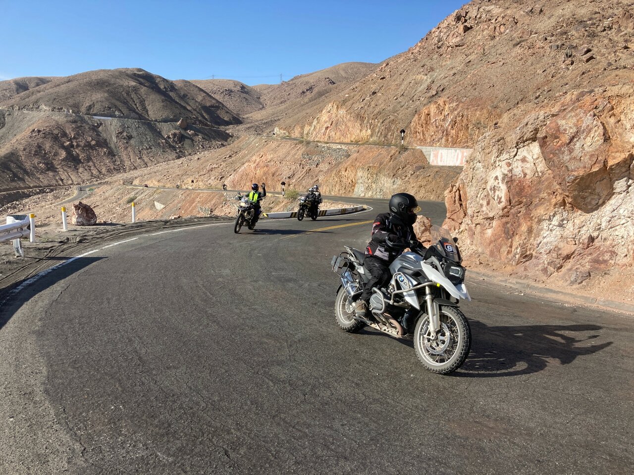 Drei Motorradfahrer auf einer Serpentinenstraße durch eine rote Felsschlucht in den peruanischen Anden