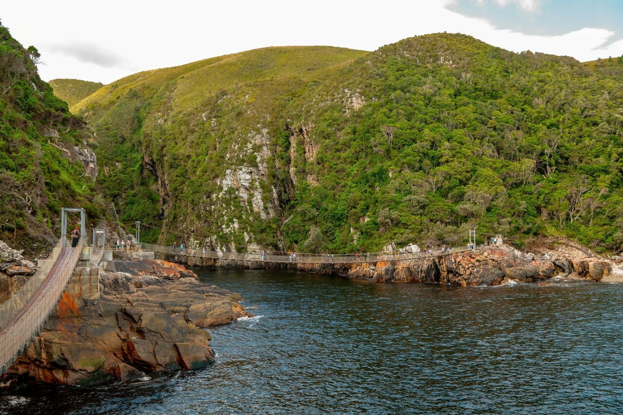 Caminhantes atravessando uma ponte suspensa sobre a foz do Storms River no Tsitsikamma National Park