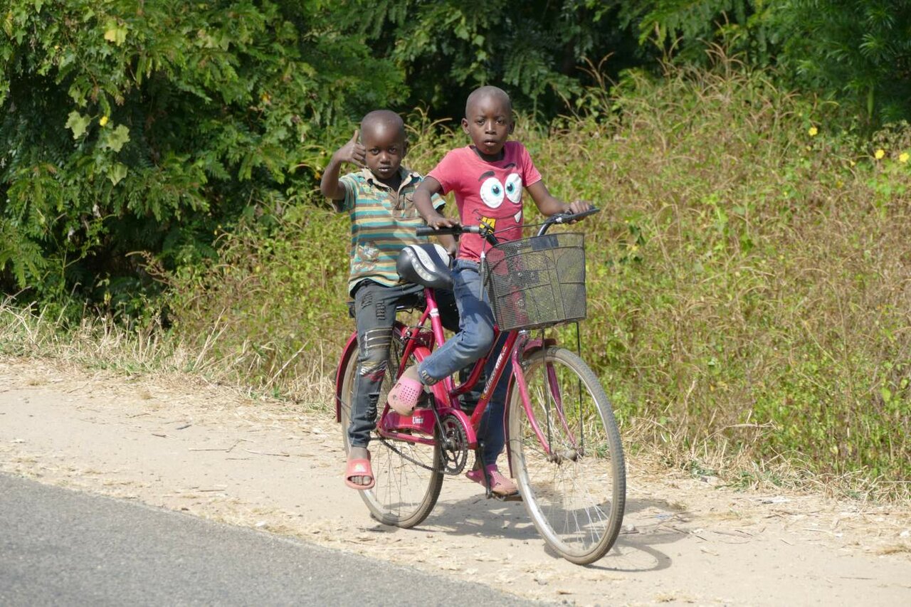 Zwei Kinder fahren gemeinsam mit dem Fahrrad neben einer Landstraße