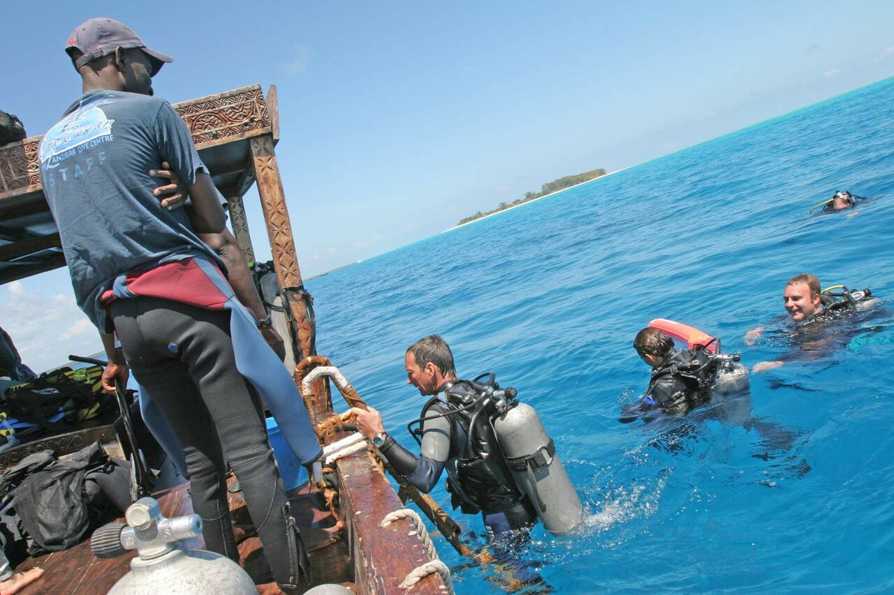 Buceadores entrando al agua turquesa desde un barco de madera cerca de una isla de arena