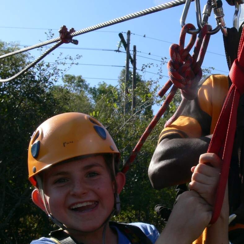 Ein lächelndes Kind mit Helm und Klettergurt beim Fahren einer Seilrutsche