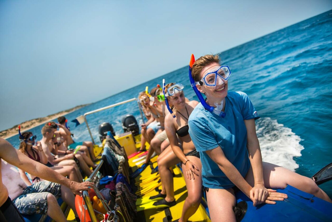 Turistas com máscaras e nadadeiras de snorkel sentados na lateral de um barco no mar