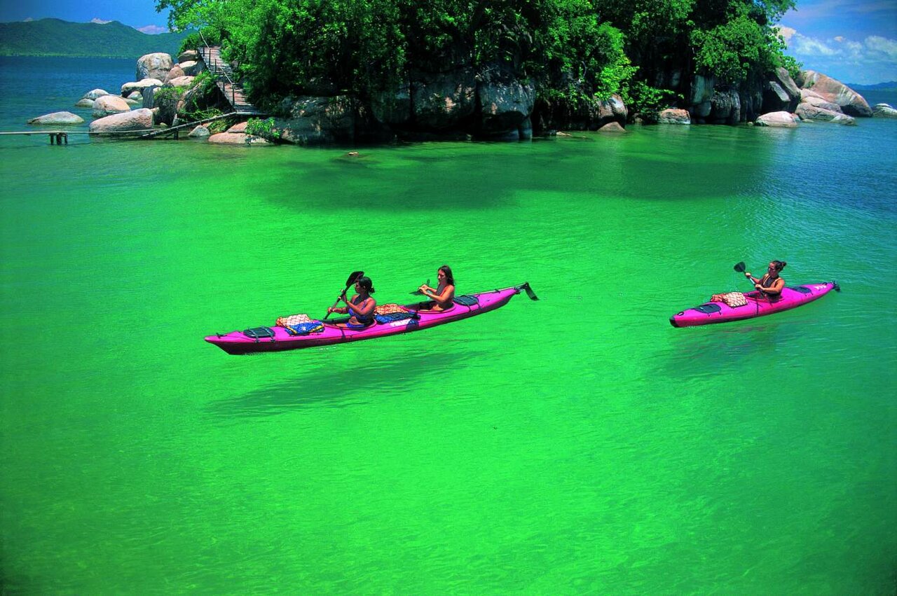Zwei Kajakfahrer paddeln auf einem See nahe einer kleinen, felsigen und bewaldeten Insel