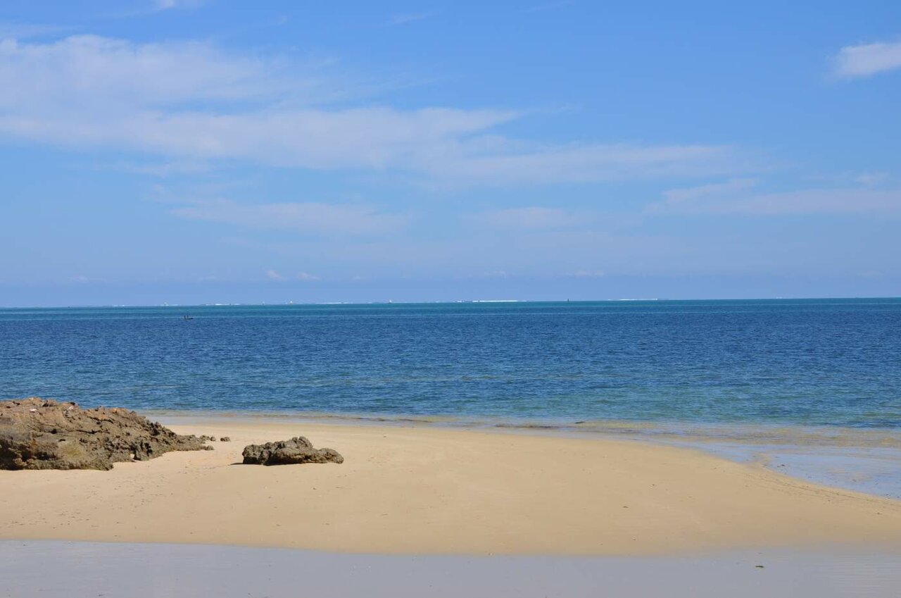 Praia de areia vazia com água turquesa encontrando um horizonte enevoado