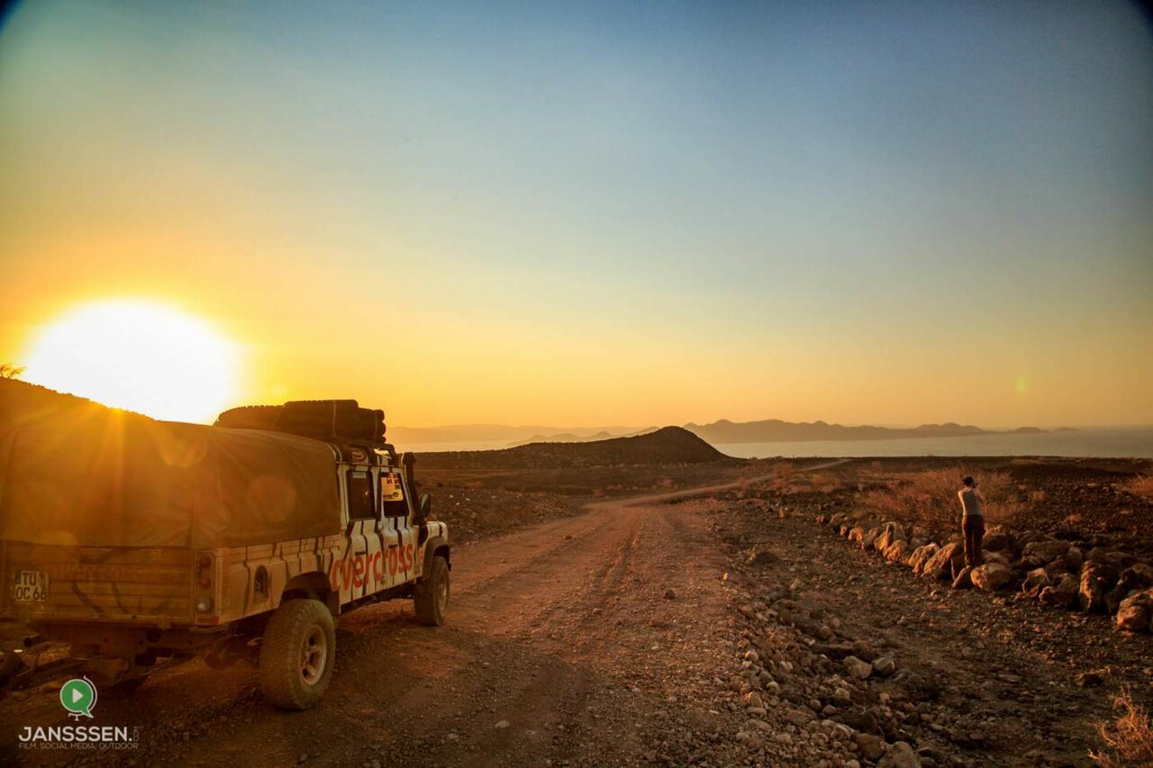Ein zebragestreifter 4x4 mit Overcross-Beschriftung steht bei Sonnenuntergang auf einer steinigen Piste