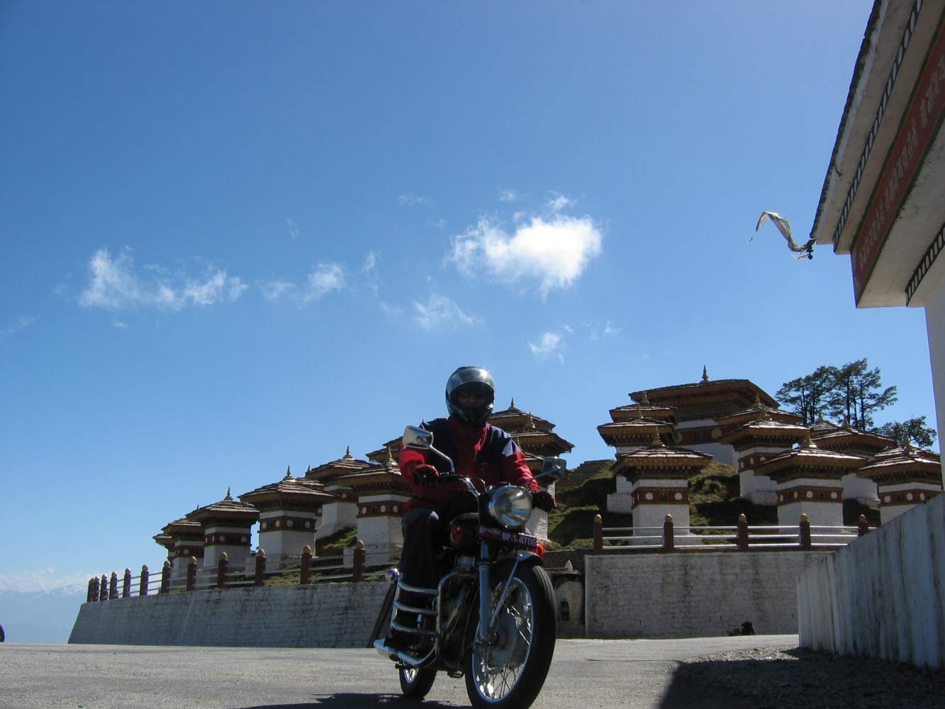 Motorradfahrer auf einer Royal Enfield vor einer Tempelanlage in Bhutan