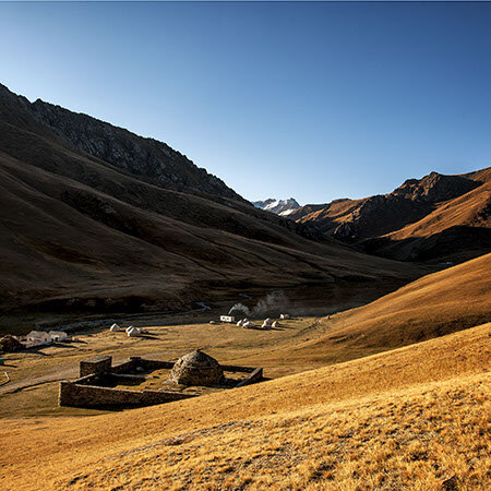 Un valle de montaña al anochecer con un pequeño poblado de piedra y un grupo de yurtas