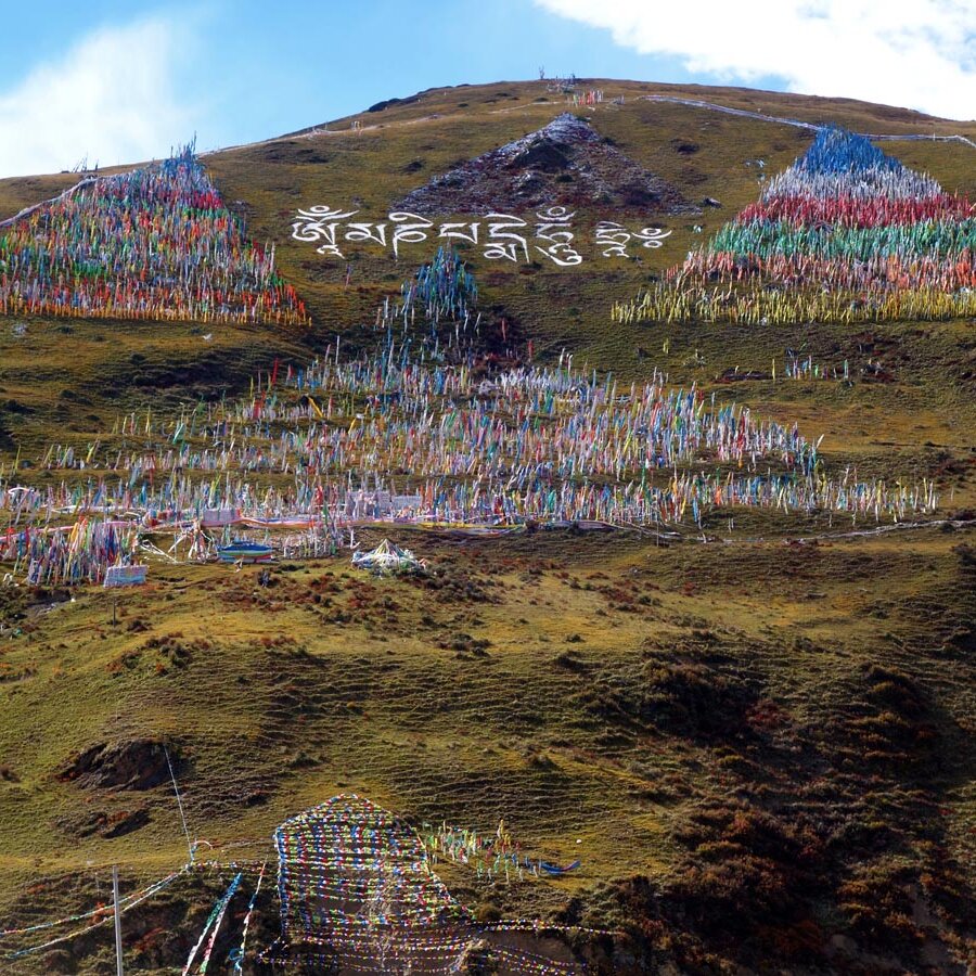 Ein Hang bedeckt mit bunten Gebetsfahnen, ein tibetisch-buddhistisches Mantra ist auf den Hang gemalt