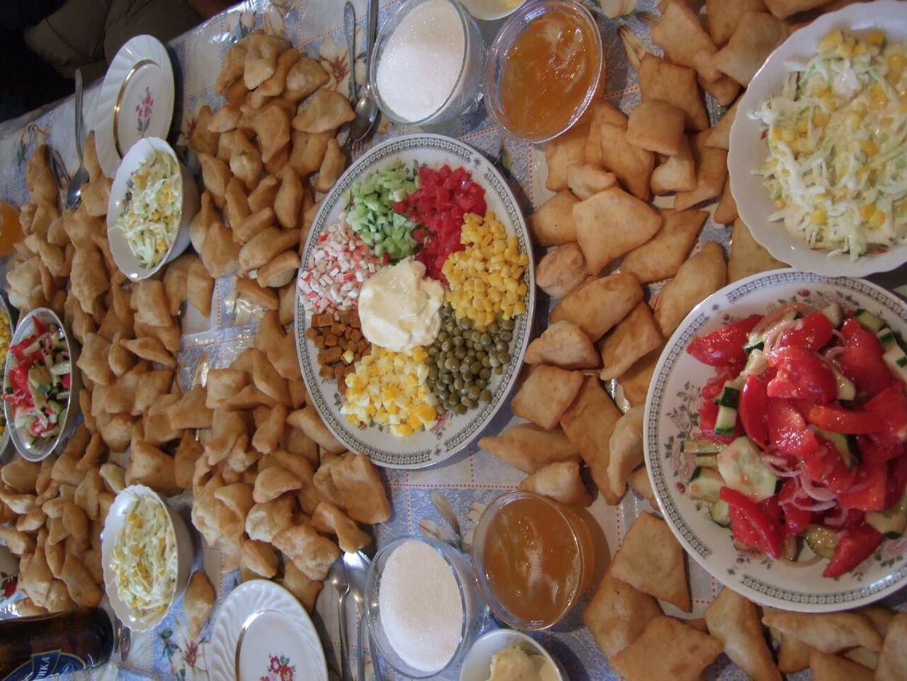 Una mesa con empanadillas fritas, ensaladas y salsas para una comida compartida
