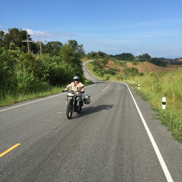 Ein Motorradfahrer winkt beim Fahren mit einer Reiseenduro auf einer asphaltierten Straße