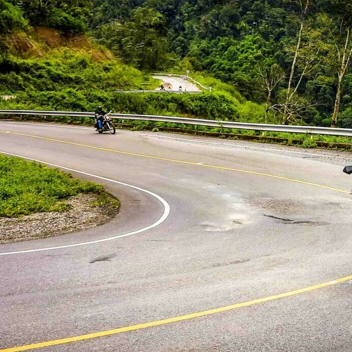 Ein rotes Motorrad in einer Haarnadelkurve am Berg, weitere Fahrer folgen auf der Straße darunter