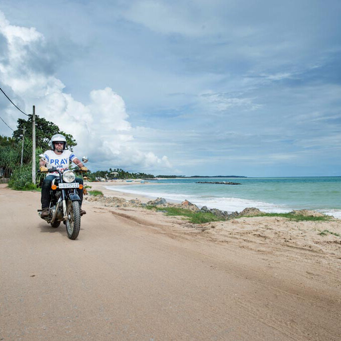Ein Motorradfahrer fährt auf einer sandigen Strandstraße am Meer entlang