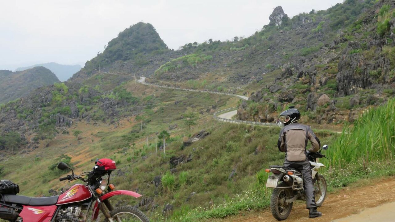 Duas motos com vista para uma estrada sinuosa por montanhas rochosas cársicas