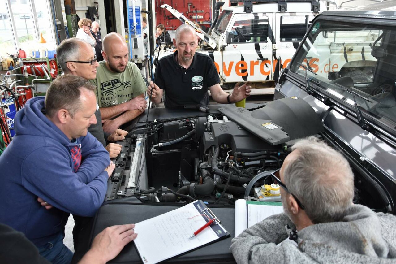 Ein Ausbilder erklärt den Kursteilnehmern den offenen Motorraum eines Land Rover Defender